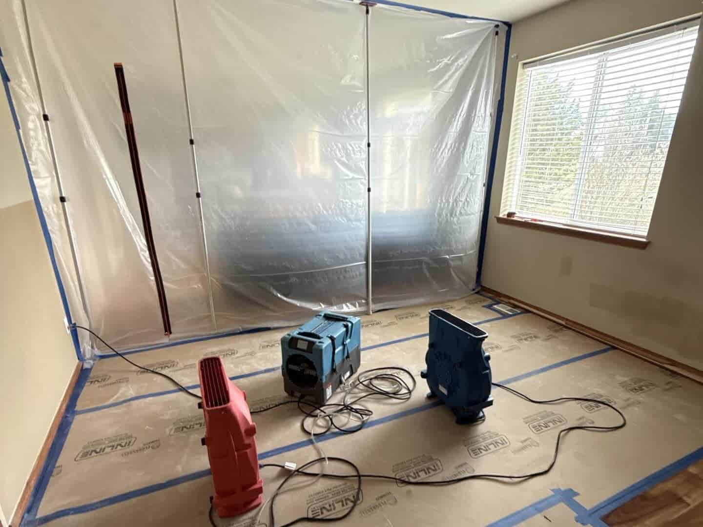 Temporary containment barrier, dehumidifier, and air movers set up for structural drying during water damage mitigation.